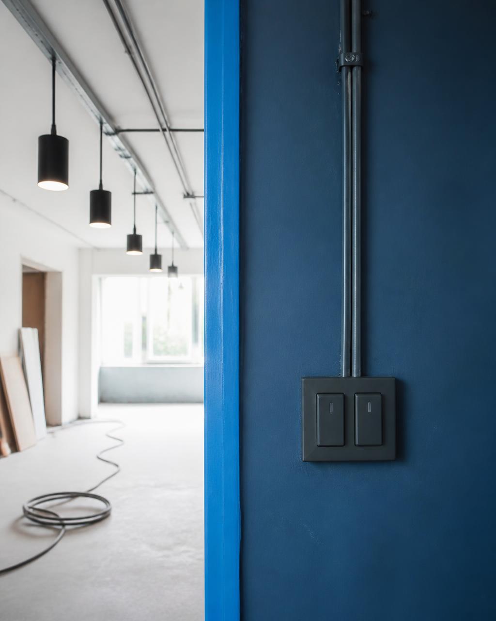Nyinstallerad strömbrytare och rörledning på blå vägg i lokal under ombyggnad